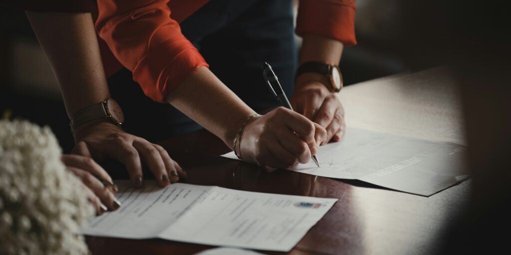 romain-dancre-doplSDELX7E-unsplash Close of the hands of tow people signing a contract.